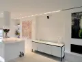 Modernt kök och vardagsrum med vita ytor, konst och spotlights som skapar en ljus och inbjudande atmosfär.