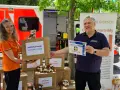 Zwei Personen vor einem Rettungswagen präsentieren Kartons für die Notfallseelsorge. Sie sind bereit, als Notfallseelsorger zu helfen.