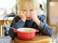 Ein Junge mit blonden Haaren stützt seinen Kopf auf die Hände und schaut lustlos auf eine Schüssel Porridge. Er isst nicht, obwohl er 10 Jahre alt ist.
