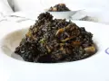 Un plato de arroz negro con trozos de calamar, servido en un cuenco blanco.