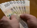 Dłonie trzymają stos banknotów po 200 zł. Czy to wystarczy, by poznać, ile wynosi najniższa krajowa netto?