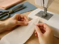 Manos cosiendo tela con puntada zigzag, aprendiendo trucos de costura a mano. Tijeras y telas a un lado.