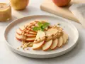 Ein gesunder Snack: Apfelscheiben mit cremiger Erdnussbutter und gehackten Nüssen, garniert mit Minze.