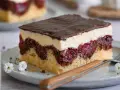 Ein Stück Donauwelle, leichte Variante, mit Schokoglasur, Sahne, Kirschen und Marmor-Biskuit auf einem Teller mit Gabel und Blümchen.