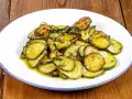 Zucchine alla poverella, fette sottili e dorate, condite con olio e erbe aromatiche, su un piatto bianco con bordo blu.