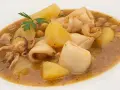 Guiso de garbanzos con trozos de calamar, patatas y perejil en un plato blanco.