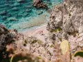Kalabria co zobaczyć: ukryta plaża z turkusową wodą, skaliste klify i dwie osoby cieszące się słońcem. Idealne miejsce na relaks.