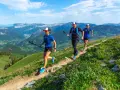Trzy osoby uprawiające speed hiking na górskim szlaku, ciesząc się pięknymi widokami.