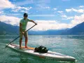 Mann auf SUP-Board mit Paddel, genießt die Geschwindigkeit auf dem See vor einer Bergkulisse.