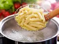 Penne w cedzaku nad garnkiem z wrzącą wodą. Prosty sposób, jak ugotować makaron do ulubionego sosu.