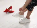 Kobieta sznuruje białe sneakersy, obok czerwone szpilki. Wkładka zmniejszająca rozmiar buta zapewnia komfort.
