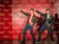 Dwie woskowe figury, jedna z odkrytym torsem, stoją na tle powtarzającego się logo Madame Tussauds w Hongkongu.