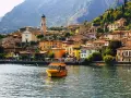 Un giallo battello solca il lago, dirigendosi verso il pittoresco borgo di Limone sul Garda, con le sue case colorate aggrappate alla montagna.