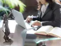 Kobieta w garniturze pracuje przy laptopie, obok Statua Temidy i otwarta księga. To droga, jak zostać prokuratorem.