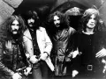 Członkowie zespołu Black Sabbath pozują do zdjęcia w mrocznym otoczeniu.