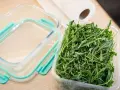 Frischer Rucola in einer Plastikschale neben einem leeren Glasbehälter. So gelingt das Rucola aufbewahren am besten.