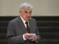 Starszy mężczyzna w garniturze, który prowadzi jeden z dziesięciu, trzyma kartkę.