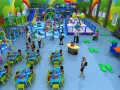 Colorata sala giochi con scivoli, piscine di palline e tavoli apparecchiati per feste di compleanno. Bambini giocano e mangiano felici.