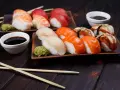 Różnorodne rodzaje sushi: nigiri z krewetką, łososiem, białym rybą i węgorzem, podane z wasabi i sosem sojowym.
