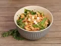 Schmackhafter Nudelsalat mit getrockneten Tomaten, Rucola und Feta in einer Schüssel auf Holzhintergrund.