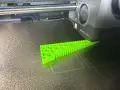 Drukarka 3D tworzy zielony obiekt z filamentu TPU, pokazując jego elastyczne właściwości.