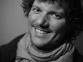 Uśmiechnięty Filip Ćwik w szarym szaliku, z kręconymi włosami i zarostem.