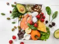 Składniki na dieta keto jadłospis: łosoś, awokado, jajka, ser, orzechy, oliwki, warzywa i gorzka czekolada.