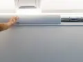 Ręka przykłada białą listwę maskującą do ściany, by ukryć plątaninę kabli. Proste rozwiązanie, jak zamaskować kable na ścianie.