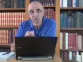 Un homme parle devant un ordinateur portable, entouré de rayonnages remplis de livres anciens, rappelant les archives départementales 85.