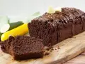 Saftiger Schoko-Zucchinikuchen mit Schokoladenglasur und zwei Herz-Dekorationen, daneben angeschnittene Scheiben und frische Zucchini.