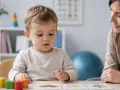 Mały chłopiec z zainteresowaniem przygląda się kartom obrazkowym, podczas gdy dorosła osoba obserwuje go z uśmiechem. To ciekawy **test AQ dla dzieci**.
