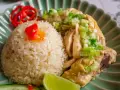 Un invitante piatto di riso con pollo, guarnito con cipollotti freschi, peperoncino rosso e una fetta di lime.