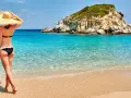 Kobieta w kapeluszu podziwia turkusowe morze i skalistą wysepkę. To widok jednej z najpiękniejszych plaż w Grecji.