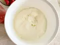 Gładki, puszysty **prosty krem z mascarpone bez śmietany** w białej misie, gotowy do deseru. Obok miski widać miseczkę z truskawkami.