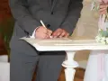 Pan młody podpisuje dokumenty, co się mówi na ślubie cywilnym? W tle panna młoda z bukietem.
