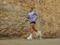 Uomo con tatuaggio corre lungo un muro di pietra. La sua tecnica di pronatore corsa è fluida e potente.