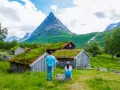 Para zwiedza ekuz w Norwegii, podziwiając tradycyjne chaty z zielonymi dachami i majestatyczne góry.