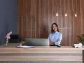 Uśmiechnięta recepcjonistka hotelowa przy ladzie. Zarobki recepcjonista hotelowy mogą być różne, ale jej postawa sugeruje zadowolenie z pracy.