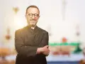 Ein lächelnder evangelischer Pfarrer mit Brille und überkreuzten Armen steht vor einem unscharfen Kircheninterieur.