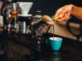 Ręka nalewa aromatyczną kawę z tygielka do turkusowej filiżanki. Idealny napój na pobudzenie przed treningiem.