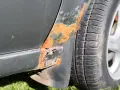 Rostfläckar och skador på bilens skärm nära däcket. En del av lacken har bubblat sig och metallen är synlig. Dags att ta bort repor på bilen och fixa rosten!