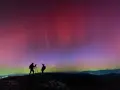 Due fotografi ammirano l'incredibile aurora boreale in Italia, con sfumature rosa e viola che danzano nel cielo stellato.