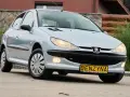 Jasny Peugeot 206 1.4 benzyna z żółtą tablicą "BENZYNA" na zderzaku, zaparkowany na zewnątrz.