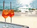Zwei Aperol Spritz Gläser mit Eis und Orangenscheiben stehen am Strand. So trinkt man Aperol Spritz in Italien!