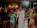 Radosna panna młoda w białej sukni tańczy z przyjaciółkami. Światła tworzą magiczną atmosferę, jakby z najlepszych **presetów**.
