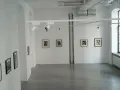 Galeria sztuki z pracami Karola Hillera. Wnętrze z białymi ścianami, szarą podłogą i kilkoma czarno-białymi fotografiami na ścianach.