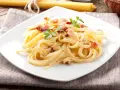 Pyszne spaghetti carbonara z boczkiem i natką pietruszki na białym talerzu.