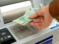 Dłoń wkłada banknoty 100 zł do bankomatu. Zastanawiasz się, ile można wpłacić na konto?