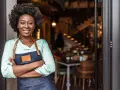 Mujer sonriente con delantal, lista para abrir su restaurante. Su plan de negocio es sólido.