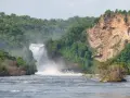 Potężny wodospad w **Uganda miasto**, otoczony bujną zielenią i skalistymi klifami. Woda spływa kaskadami do rwącej rzeki.